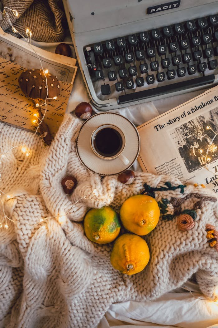 A warm, cozy setup featuring a typewriter, coffee, lemons, and fairy lights.