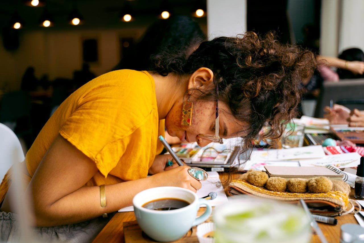 Woman engrossed in calligraphy work, enjoying coffee in a cozy indoor workshop.